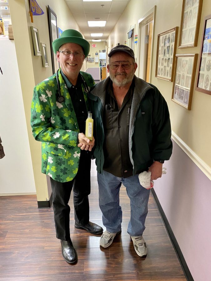 Dr Seretis in St. Patrick's day jacket and hat holding hand of older male patient